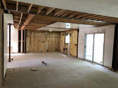 Wide-angle view of a residential interior during demolition, showing exposed ceiling joists, wall insulation, and temporary structural supports.
