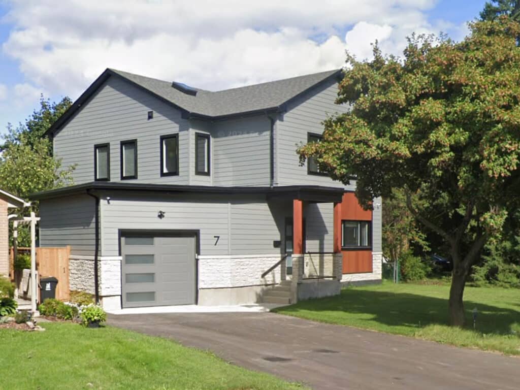 Exterior of a grey-sided house featuring a modern multi-level roofline, stone water table, and an integrated garage.