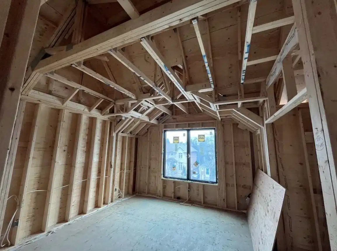 Unfinished interior room layout featuring exposed wood stud walls, complex vaulted ceiling truss framing, and a dark-framed window.