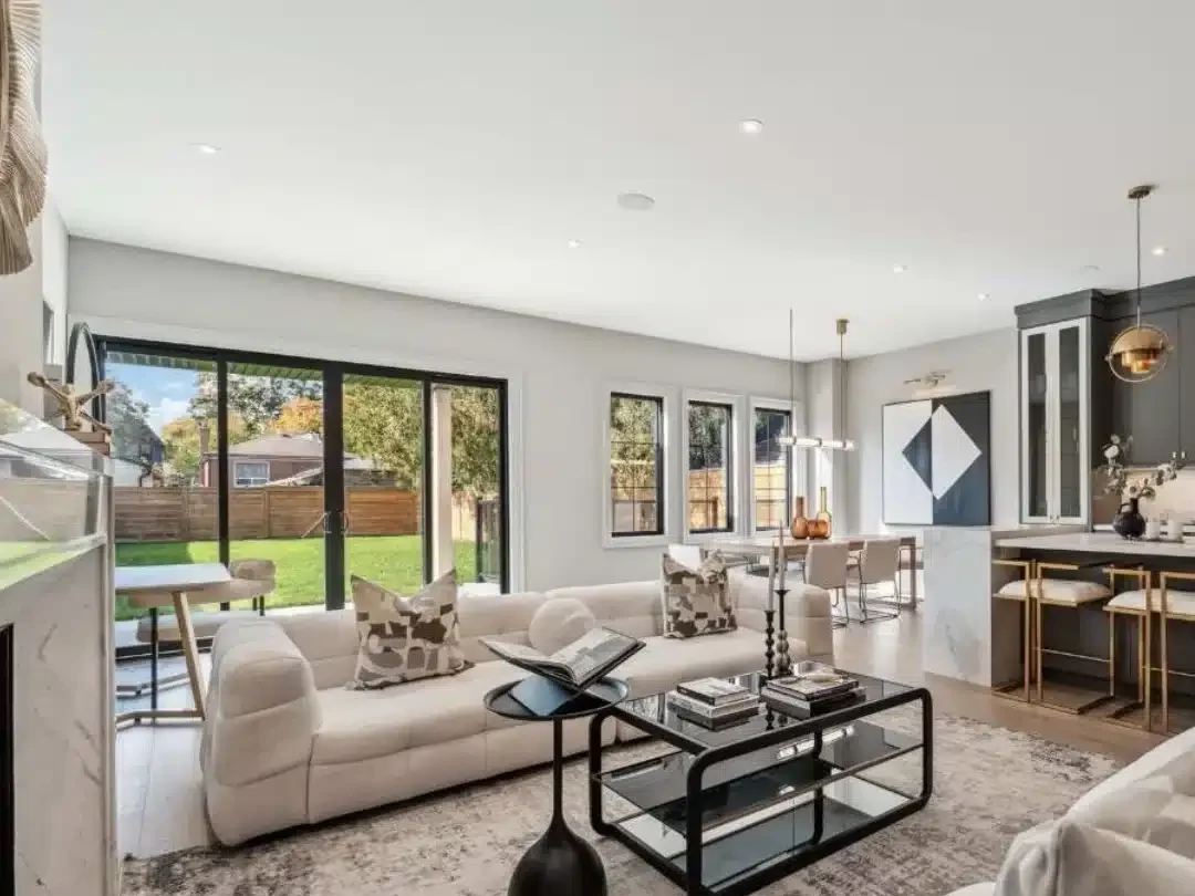 Open-concept living room and kitchen layout featuring contemporary white sofas, a marble-clad kitchen island, dark cabinets, and clear flush ceilings across a long span.