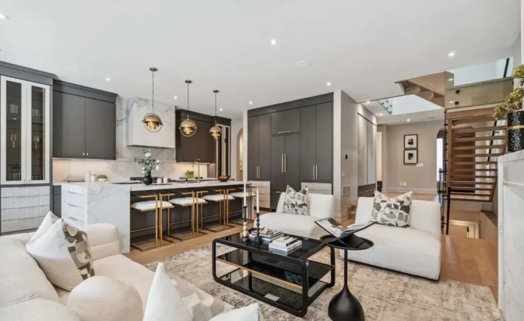 Open-concept living room and kitchen layout featuring contemporary white sofas, a marble-clad kitchen island, dark cabinets, and clear flush ceilings across a long span.