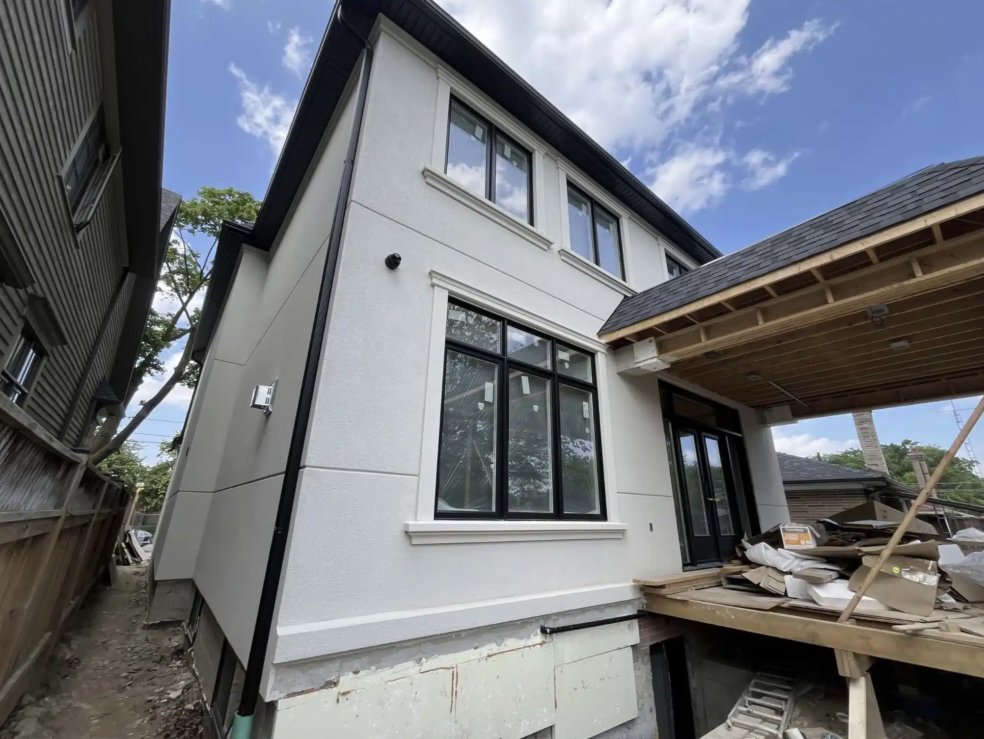 Side exterior view of a modern custom residential dwelling with an attached wooden deck ledger and subfloor platform framework under structural construction.