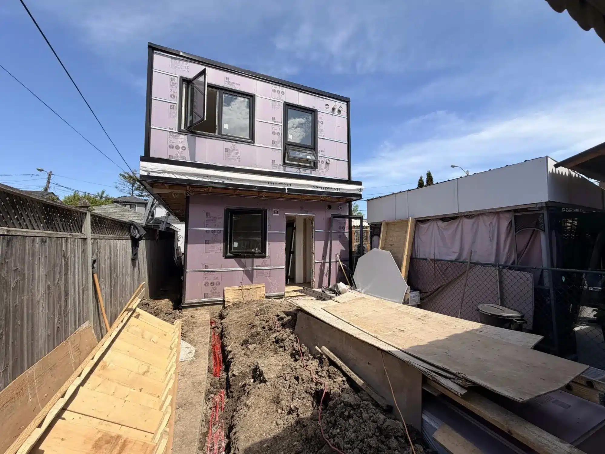 Backyard construction site of a custom laneway suite accessory structure in Toronto showing open trenching for services and foundation preparation.